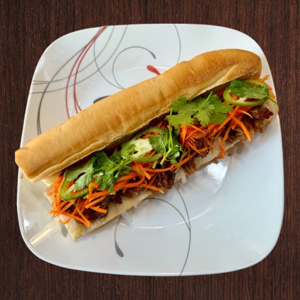 Vietnamese Banh Mi sandwich with meat, pickled carrots, cilantro, and jalapeños on a white plate.