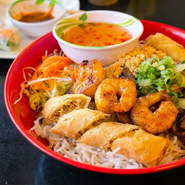 Vietnamese vermicelli bowl with grilled shrimp, spring rolls, beef, and vegetables, with sauce.