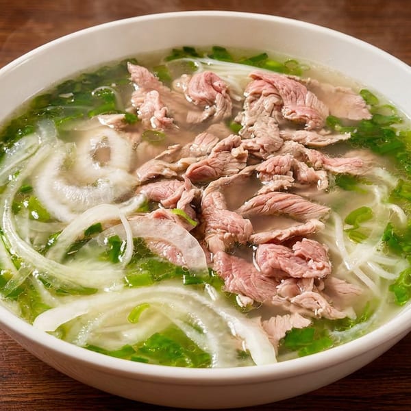 Steaming bowl of pho with sliced beef, rice noodles, green onions, and white onions in clear broth.