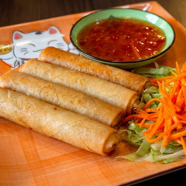 Four golden spring rolls, sweet chili sauce, and fresh salad on an orange lucky cat plate.